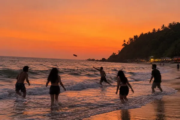 Friends throw a frisbee in the waves at sunset on a beach in Gokarna